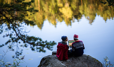 Fotograf: Sakari Piippo Bildbanken Finland Två vandrare sitter på klippan vid sjön med en laptop i handen.