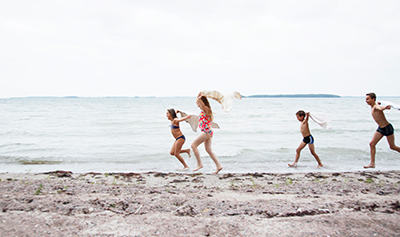 Fotograf: Katri Lehtola Bildbanken Finland Barn springer på stranden i baddräkter med handdukar.
