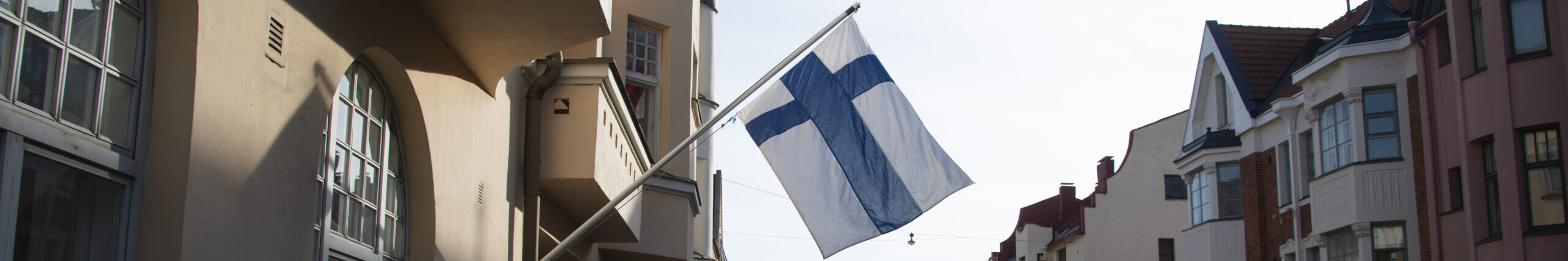 Kuvaaja: Jarno Mela. Suomi-kuvapankki Suomen lippu liehuu kadulla, jossa on vanhoja taloja.